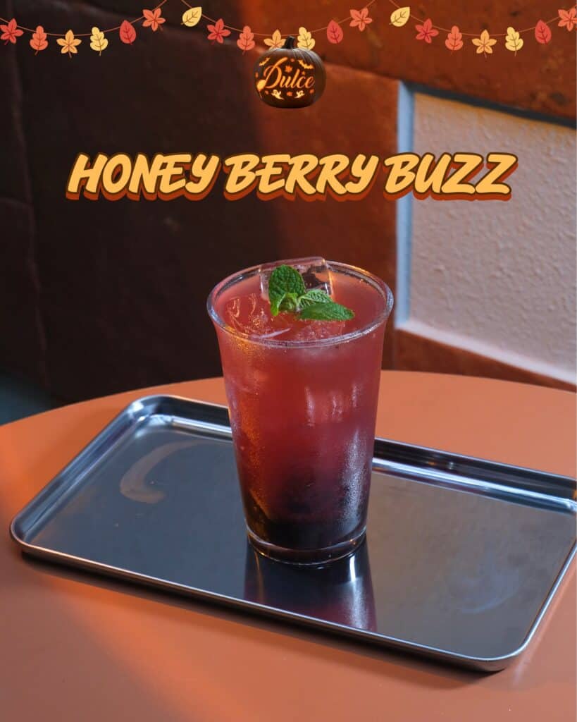 Honey Berry Buzz, a red-to-purple iced soda with a mint sprig and a large ice cube on a steel tray at Dulce de Saigon