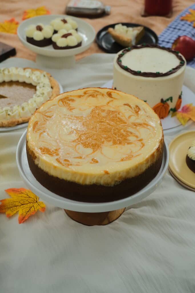 Whole Pumpkin Cheesecake with an orange and cream marbled swirl top on a cake stand at Dulce de Saigon